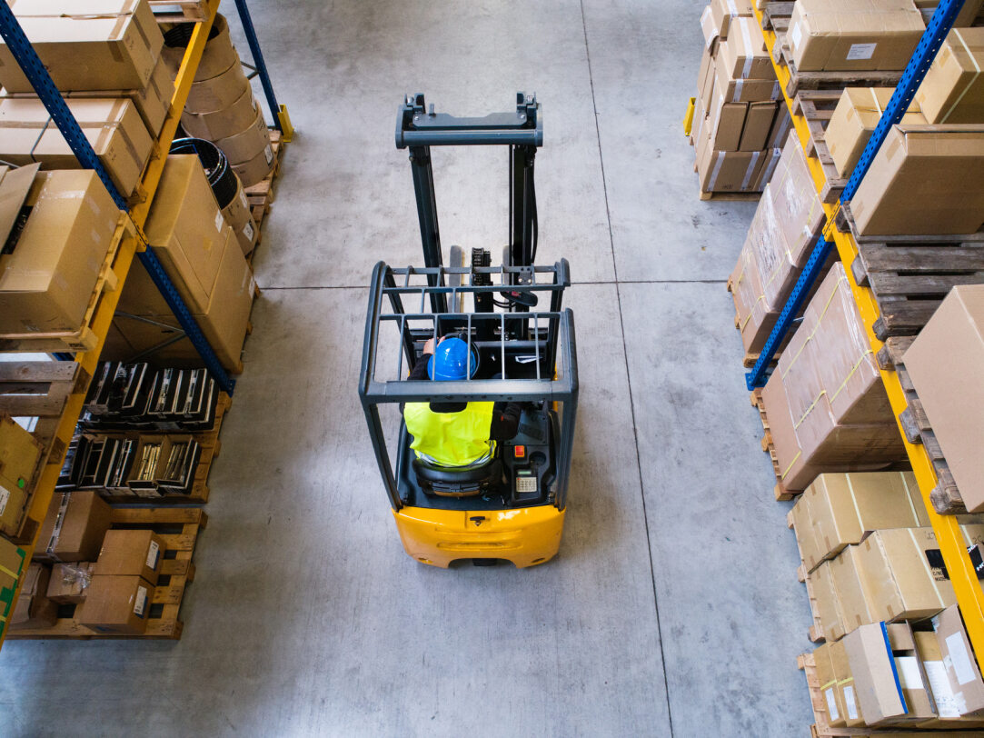 Used forklift being driven through a warehouse by a person with a yellow vest