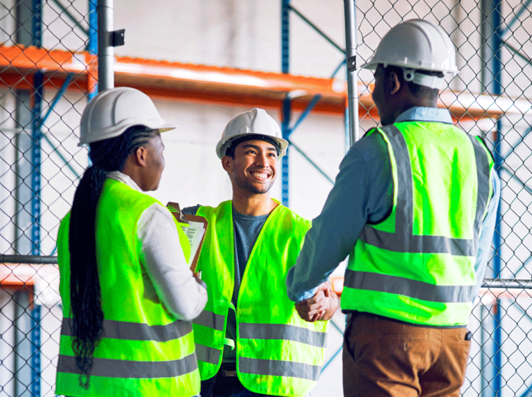 Three people working in a warehouse with hard hats and safety vests